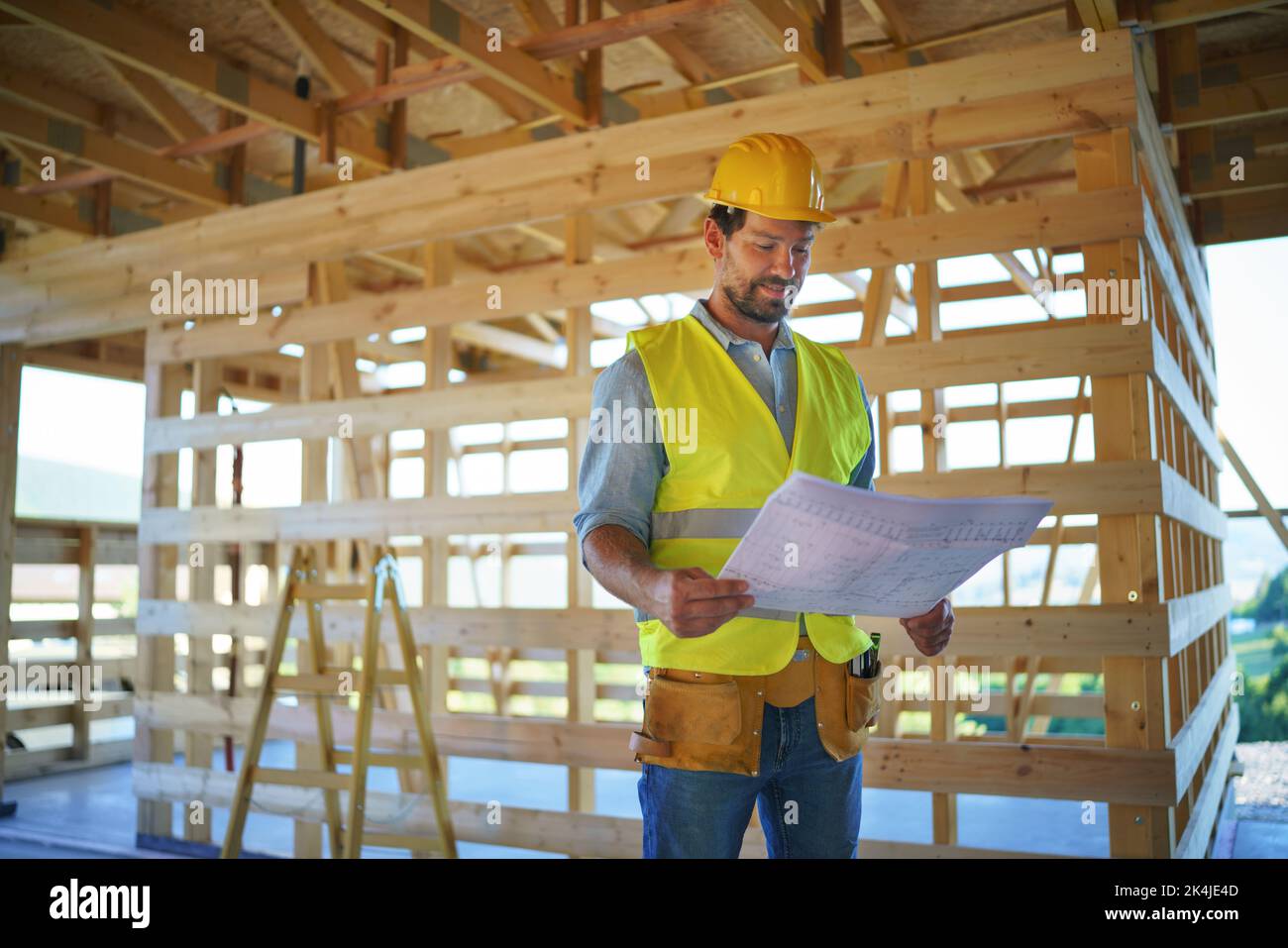Construction engineer or architect with blueprints visiting and chechking eco building site of wood frame house. Stock Photo