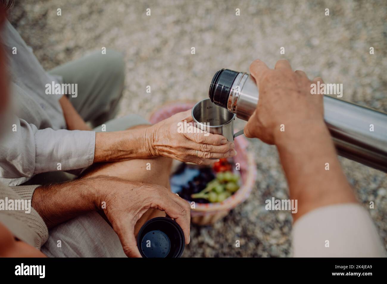 Close-up of senior couple having picnic at beach during autumn day, drinking hot tea from thermos. Stock Photo