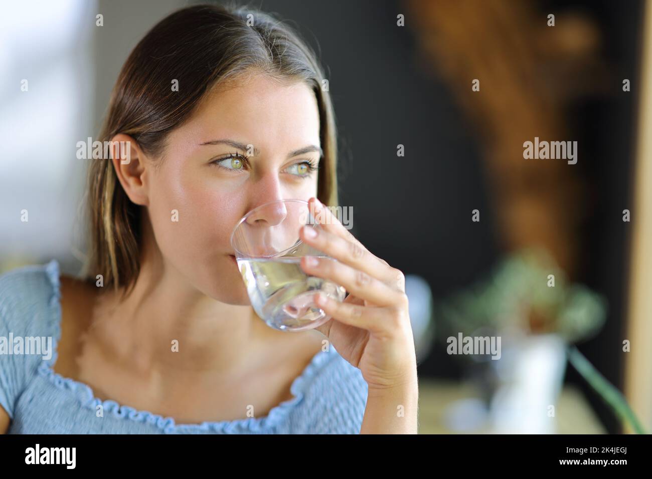 Happy woman drinking water from glass contemplating at home or restaurant Stock Photo