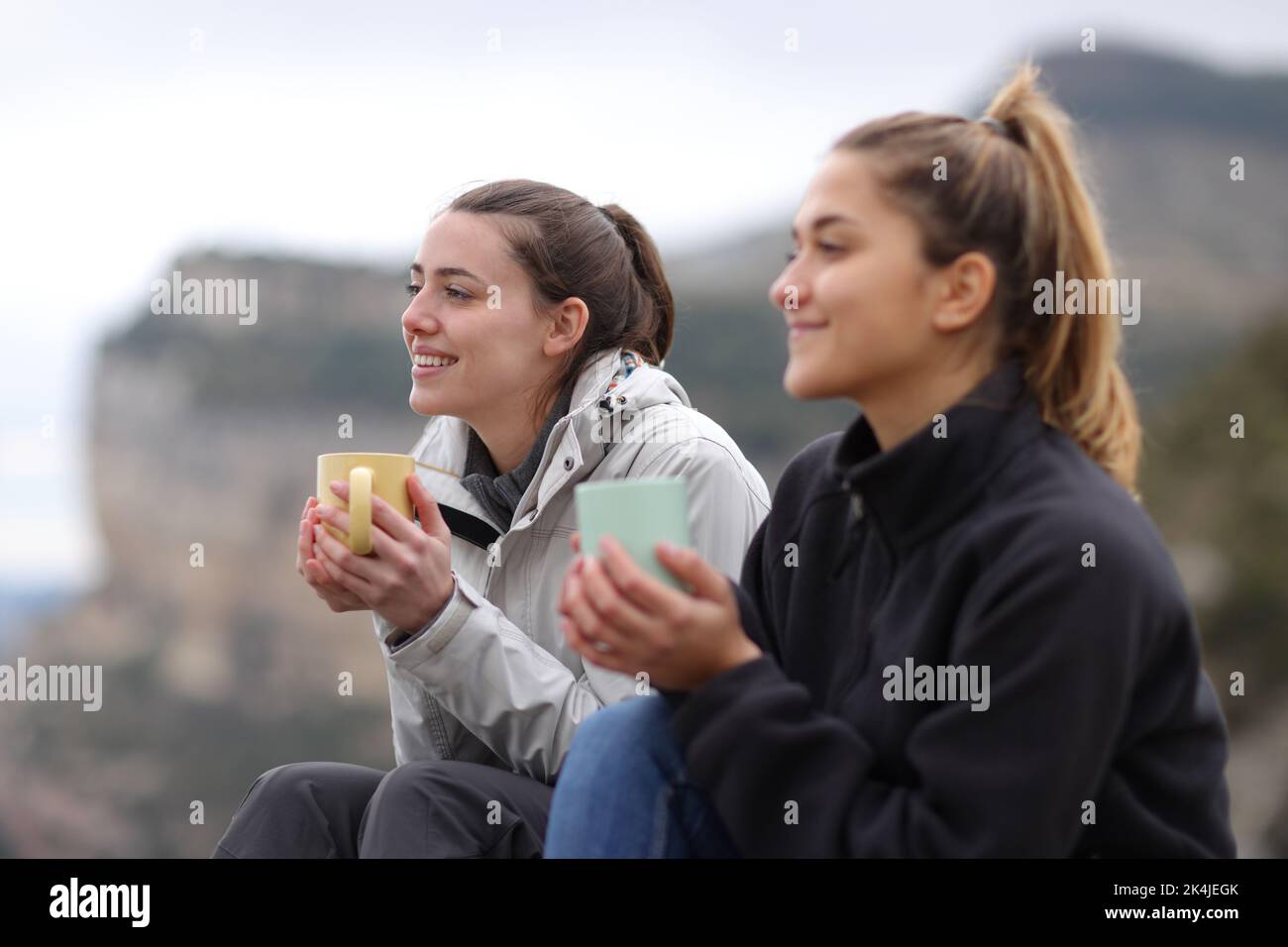 Two trekkers drinking coffee sitting in the mountain looking away Stock Photo