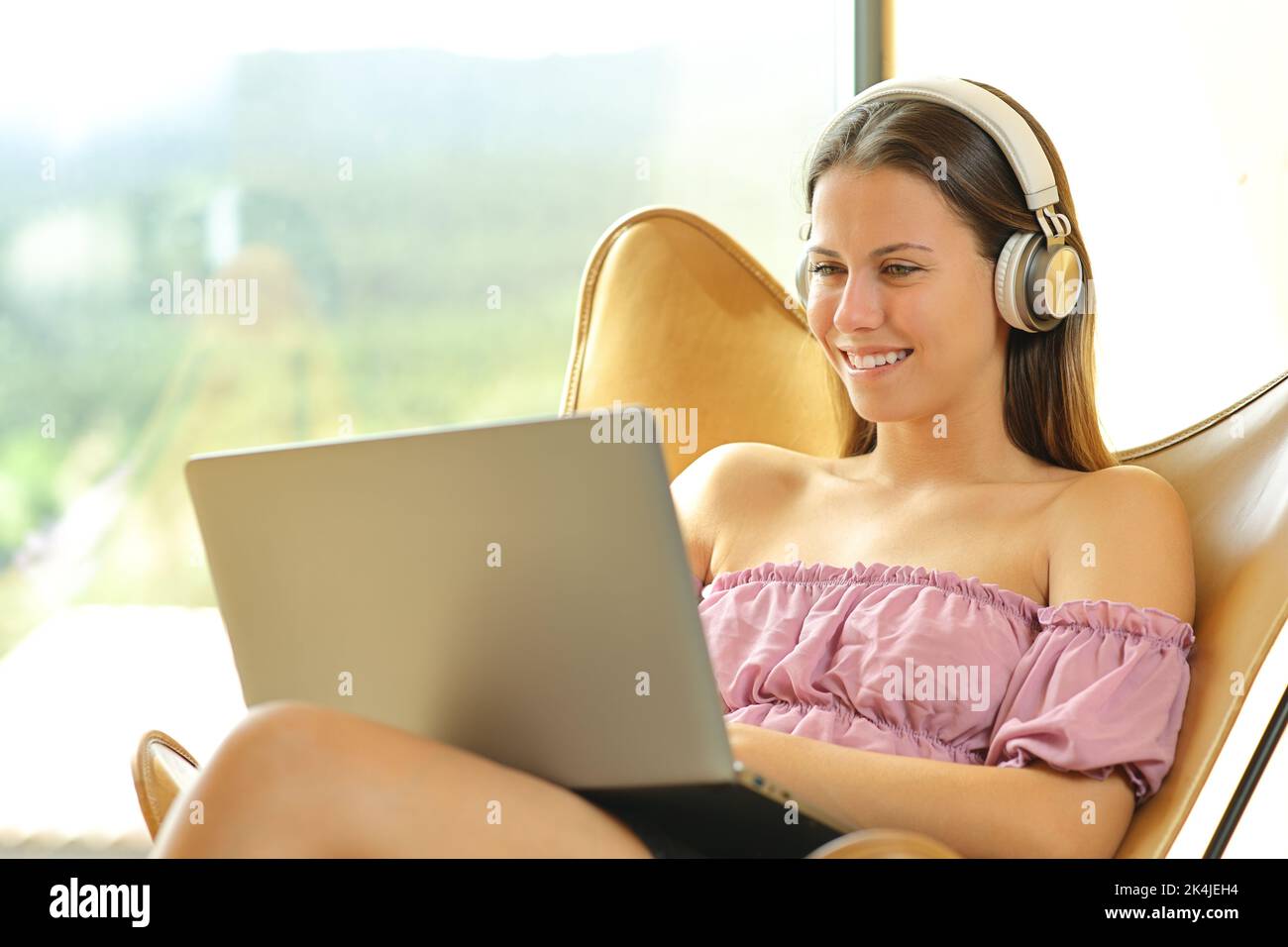 Happy woman watching media on laptop sitting on a chair near a window at home Stock Photo