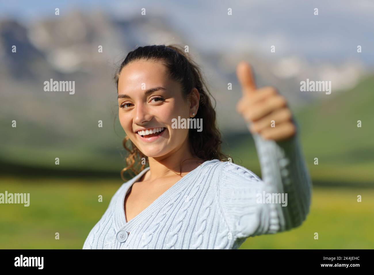 Happy woman gesturing thumbs up looking at camera in the mountain Stock Photo