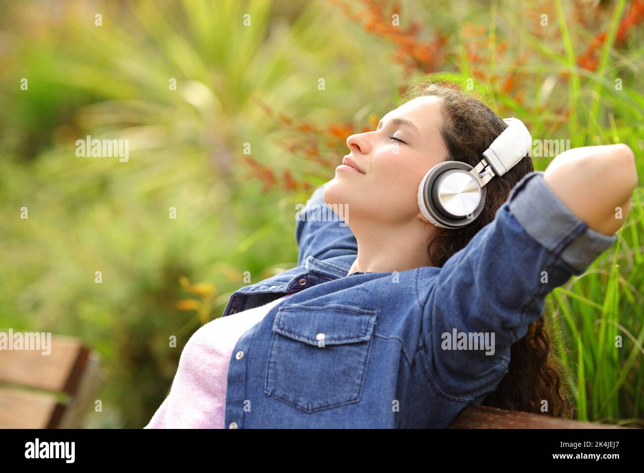 Profile of a woman relaxing with music sitting in a bench in a park Stock Photo