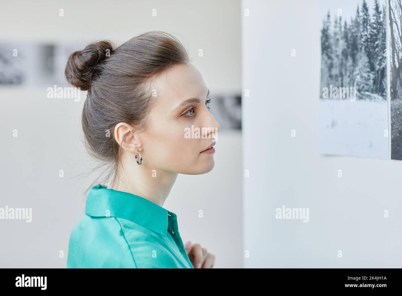 Minimal side view portrait of young woman with messy bun looking at art in gallery or museum Stock Photo