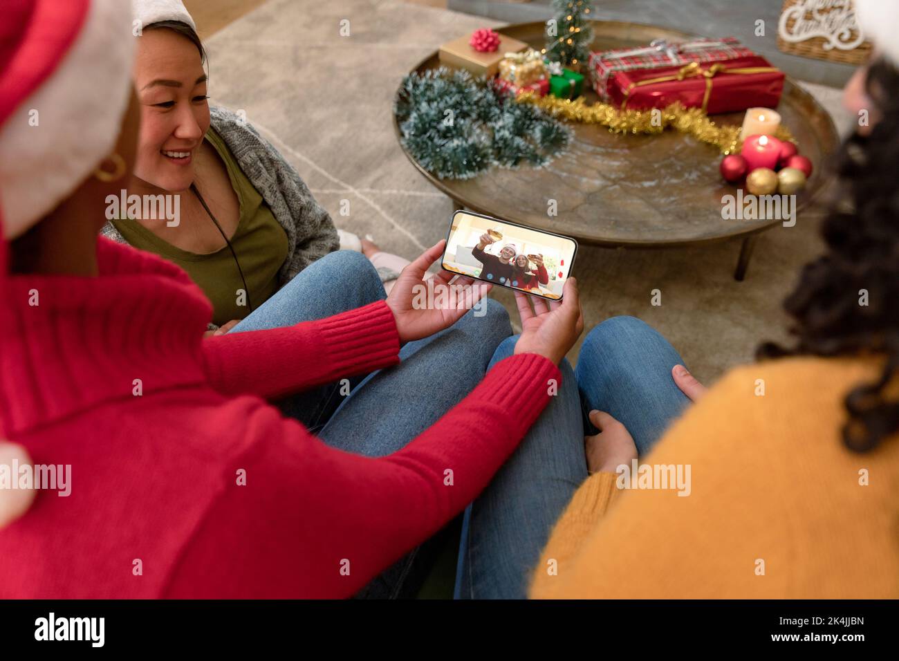 Biracial female friends on smartphone christmas video call with friends. christmas, festivity and communication technology. Stock Photo