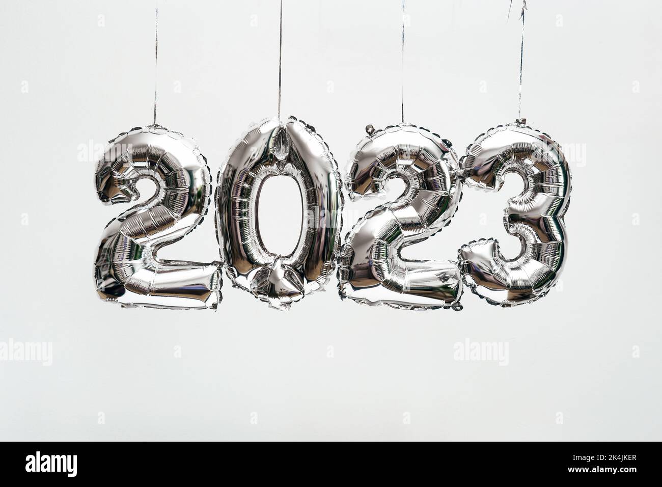 Silber foil balloons in numbers shape 2023 hanging against white wall. Stock Photo