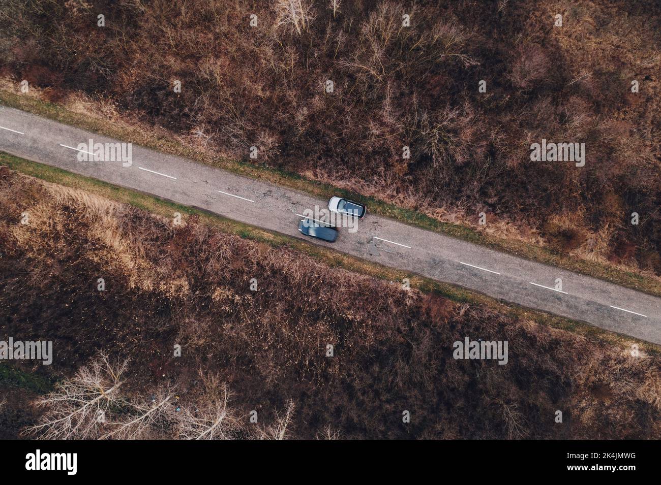 Top view drone photography of car overtaking the parked automobile along the road through wooded landscape in autumn afternoon, vehicle insurance conc Stock Photo