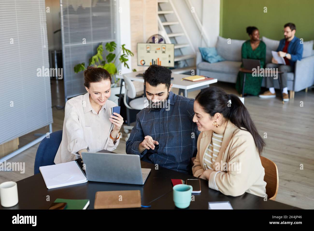 Confident man pointing at laptop screen while discussing data or video with two young female colleagues watching online training Stock Photo
