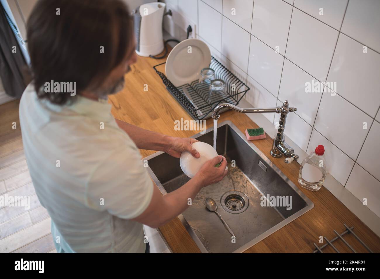 Man in the kitchen washing the dishes and doing some housework Stock Photo