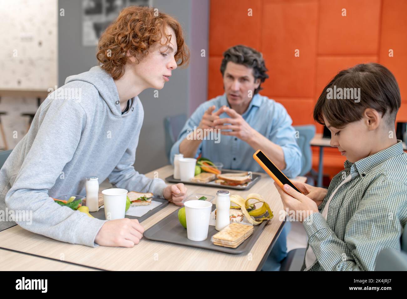 Schoolteacher conversing with two schoolboys at lunch Stock Photo