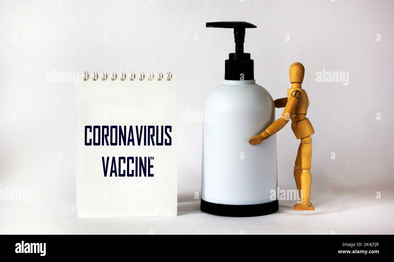Notepad with text Coronavirus Vaccine on a white background with a wooden doll and with a bacterial agent Stock Photo