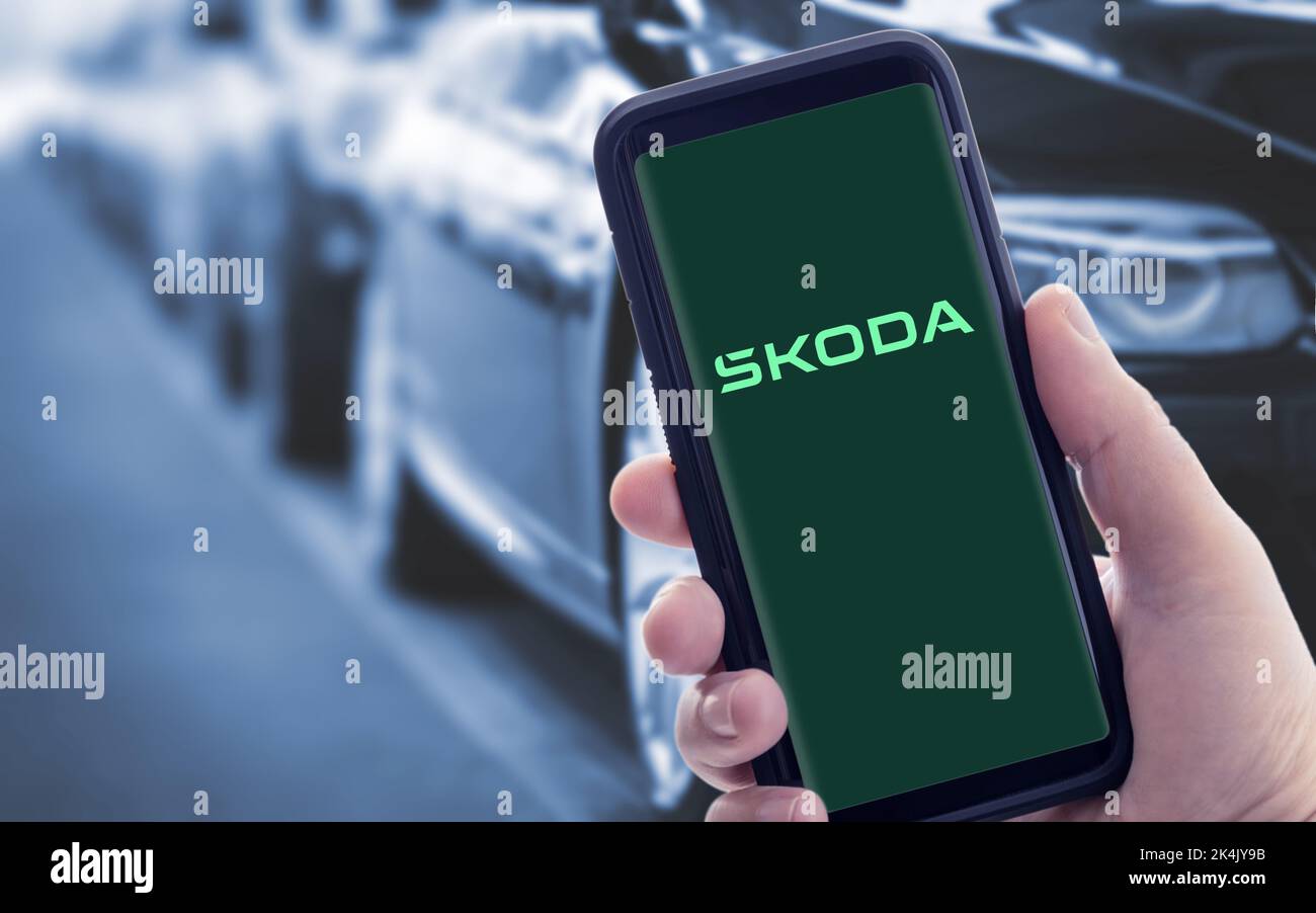 Galicia, Spain; january 09 2021: Hand holding a smart phone with new SKODA logo on screen. Blurry cars at background Stock Photo