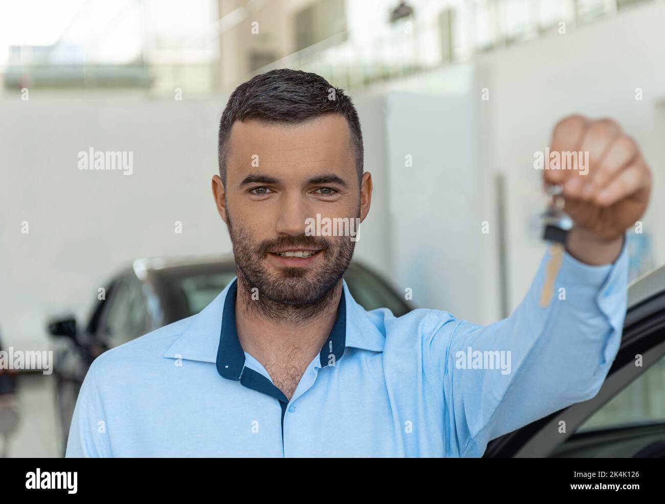 Smiling man customer holding key stands on the background of car in
