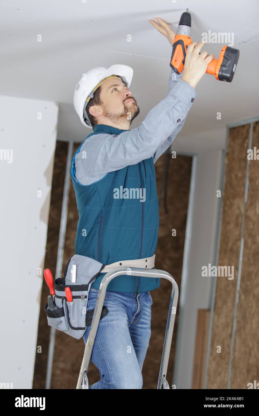 male builder drills a hole in the ceiling Stock Photo