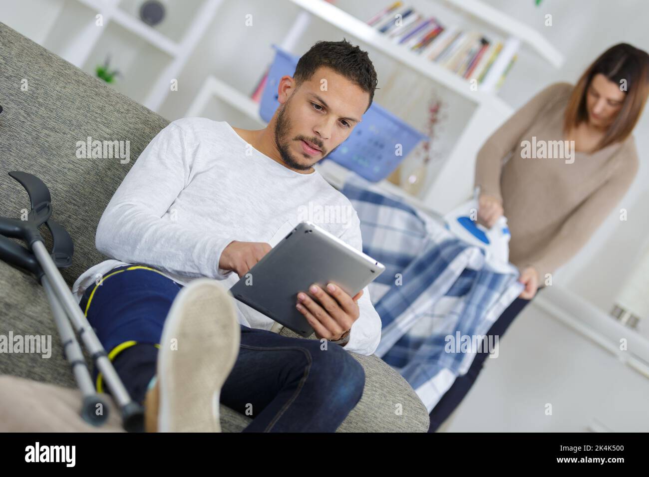 man using tablet while woman irons behind Stock Photo