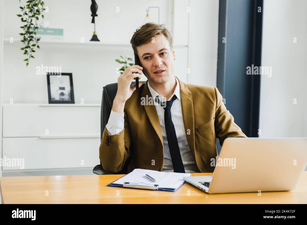 Smiling confident mature businessman leader talk on phone and sit on table in office, happy and modern business man Stock Photo