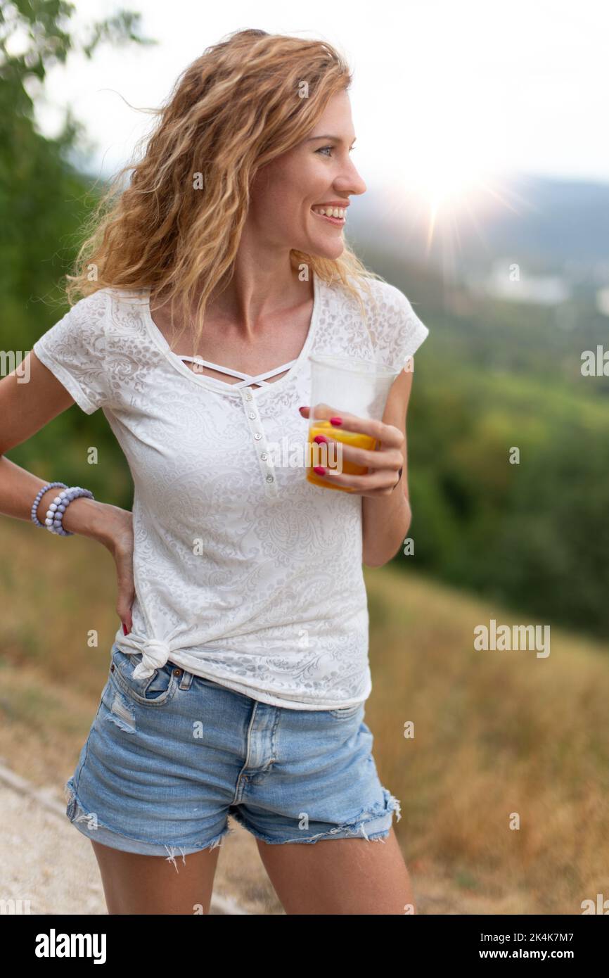 Happy young Caucasian 30s carefree woman holding glass of juice in nature Stock Photo