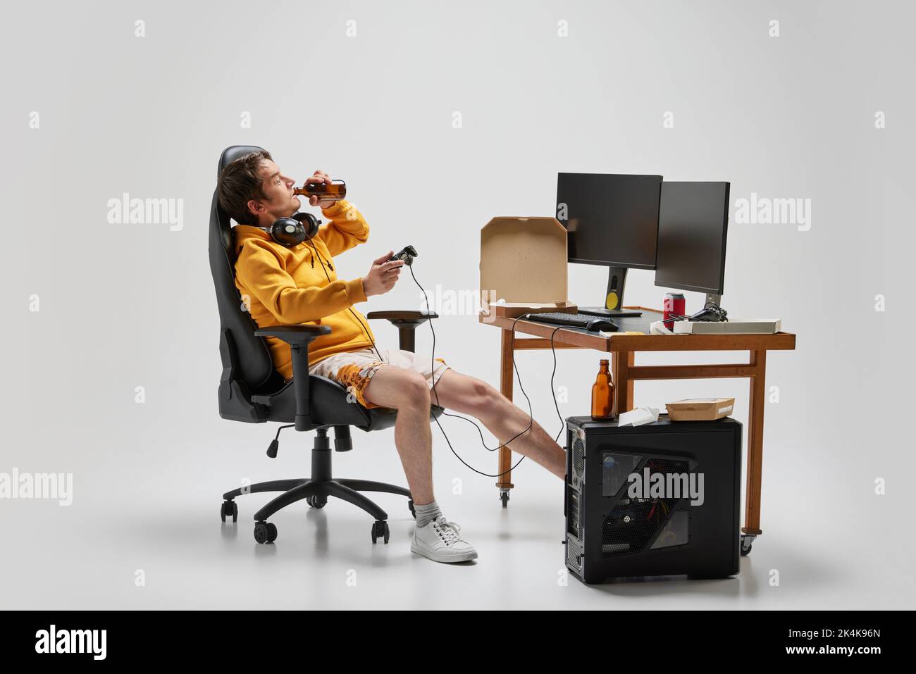 Emotional man, student sitting at home, playing computer games isolated over grey background. Hobby, studying, education, youth, remote workplace Stock Photo