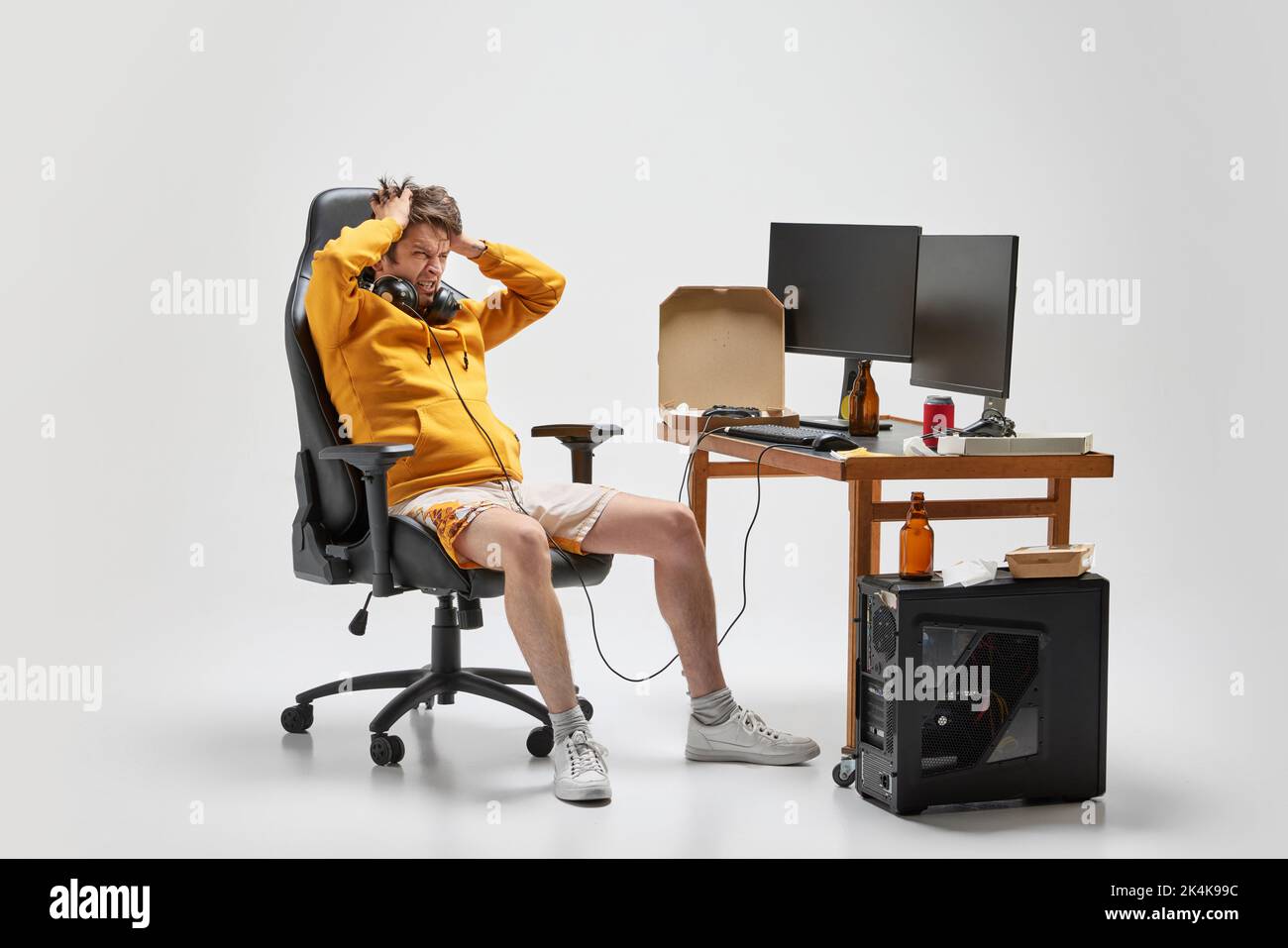 Emotional man, student sitting at home, playing computer games isolated over grey background. Hobby, studying, education, youth, remote workplace Stock Photo
