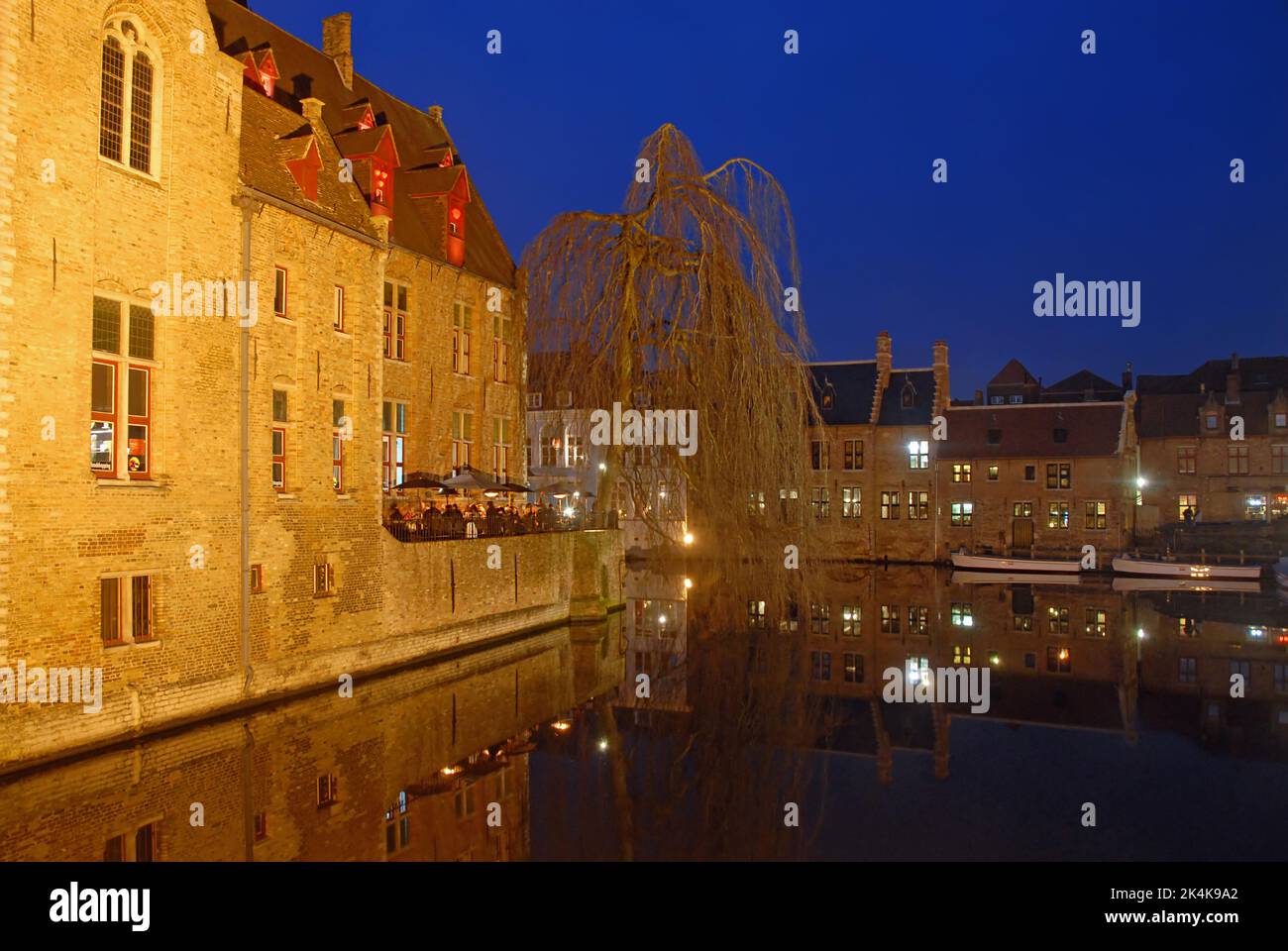 Brugge or Bruges, West Flanders, Belgium: Traditional buildings along the Dijver Canal in Brugge at night with outdoor restaurant. Stock Photo