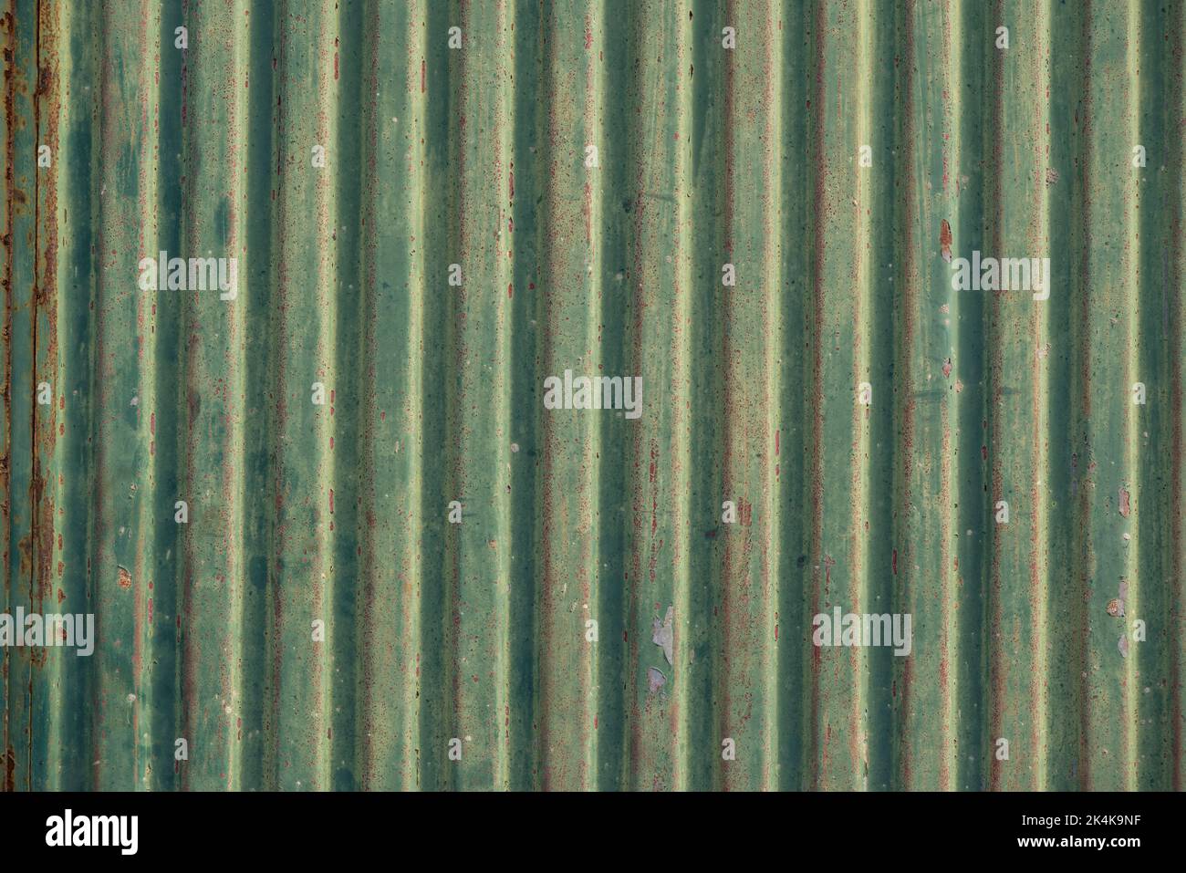 Industrial background texture, showing a weathered corrugated metal gate with rust and peeling green paint Stock Photo