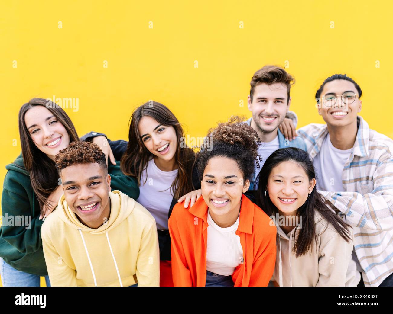 Group portrait of young multiethnic student friends against yellow wall Stock Photo