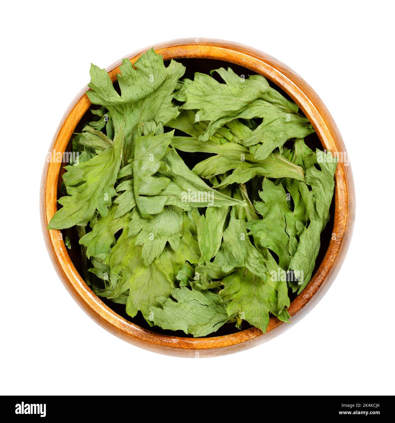 Celery, dehydrated green leaves, in a wooden bowl. Apium graveolens var. graveolens, root vegetable, primarily grown for its stalk. Stock Photo