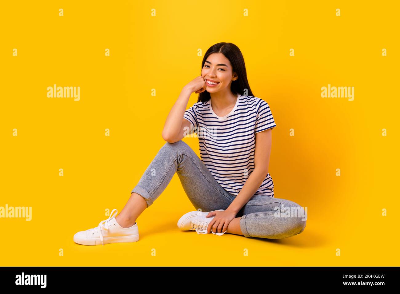 Full size photo of adorable satisfied filipino lady sit floor arm touch cheek toothy smile isolated on yellow color background Stock Photo