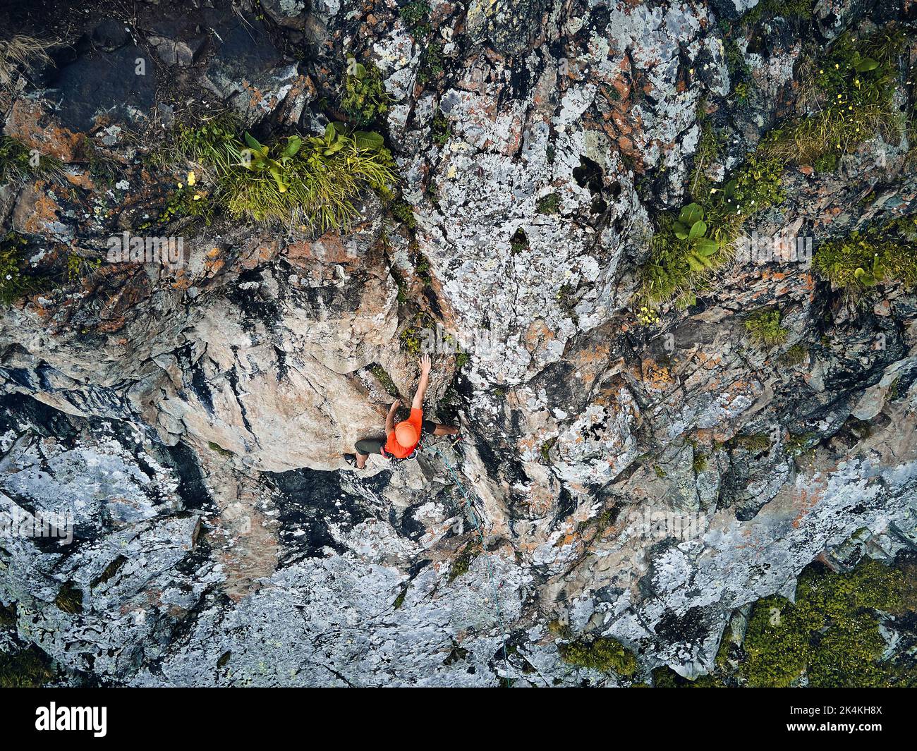 Fit strong man athlete in red shirt rock climbing on the high vertical wall at the mountains Tyan Shan in Kazakhstan. Drone shot aerial top view Stock Photo