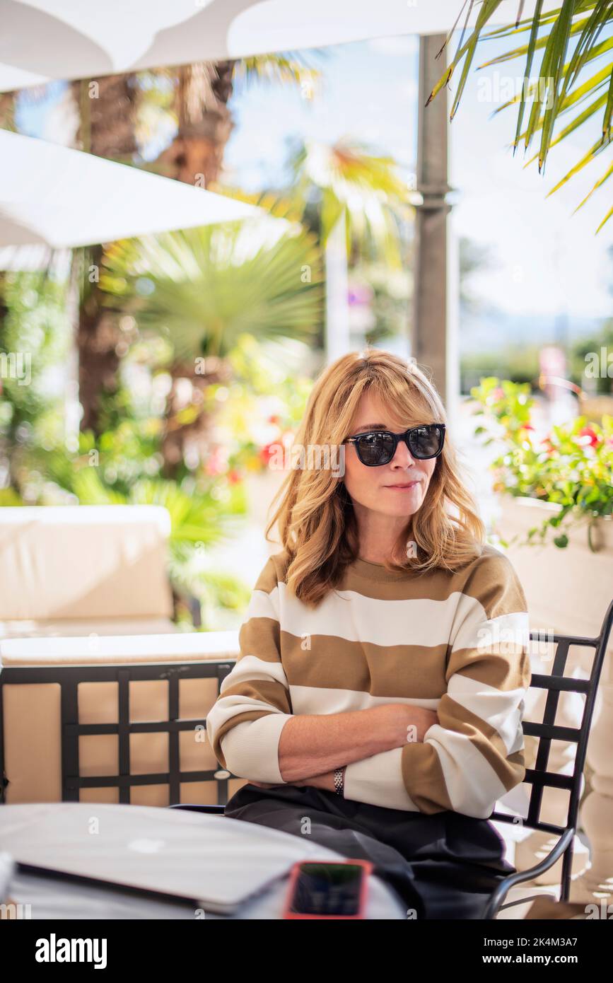 Portrait of confident middle aged woman wearing sunglasses and casual clothes while relaxing at oudoor cafe in the city. Stock Photo