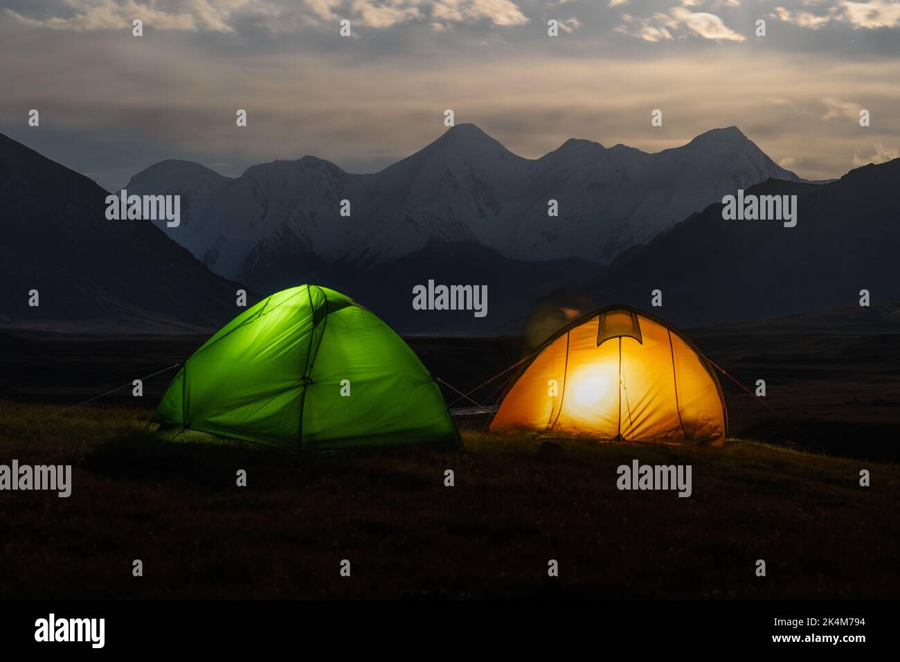 Colourful tents with lights under moonlit landscape of Sary Jaz Valley at night, Kyrgyzstan, Tien Shan mountains Stock Photo