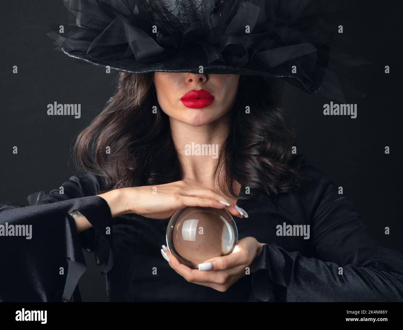 Beautiful sexy model woman in Halloween witch costume holding crystal ball putting spell fortune telling Stock Photo