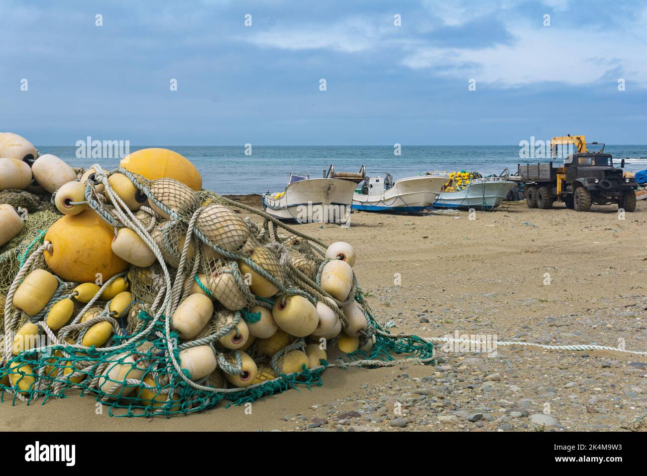 industrial fishing net with bright floats is folded on the seashore against the backdrop of fishing boats and truck crane for catch Stock Photo