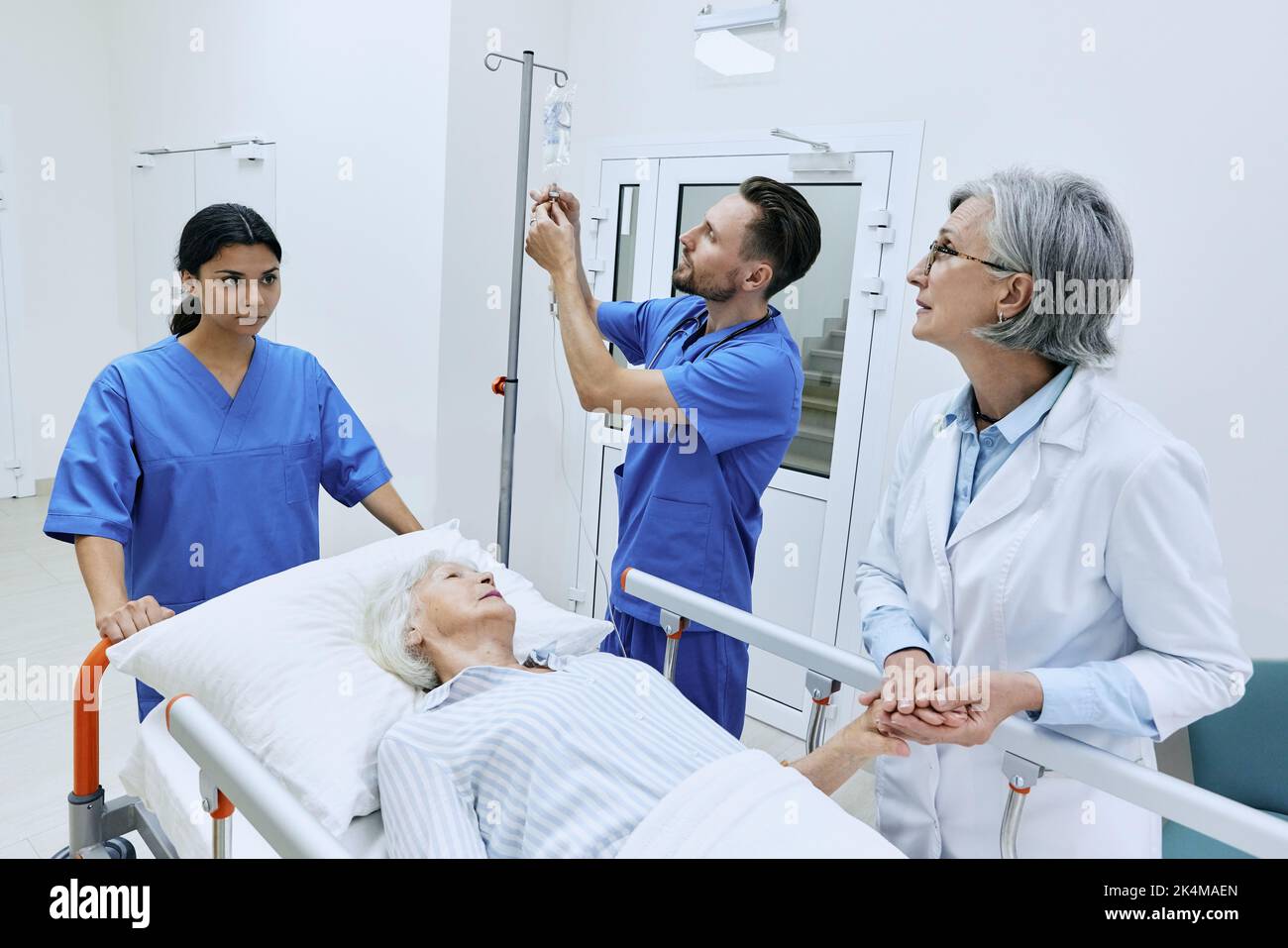 Nurse putting drip on elderly patient lying on gurney while being examined by experienced woman doctor. medical assistants will take injured woman to Stock Photo