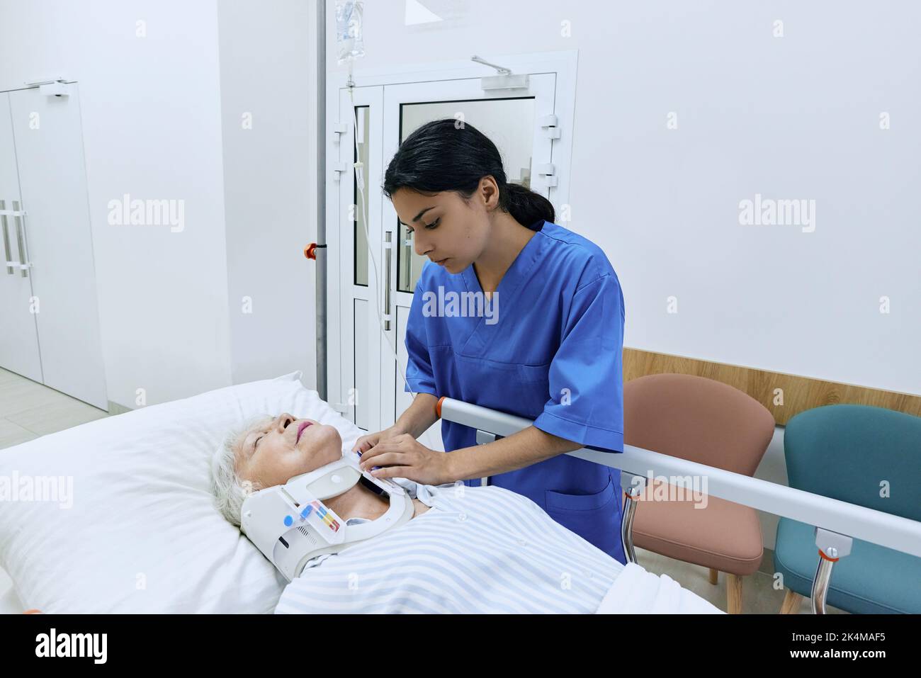 Nurse putting cervical collar on female injured neck lying on hospital gurney. Senior woman patient has acute spinal cord injury and is taken care of Stock Photo