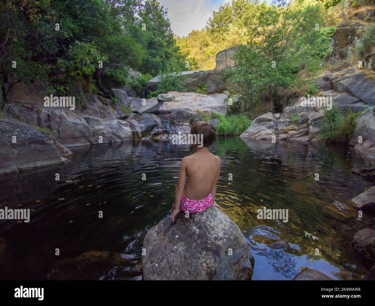 Child boy sitting at upriver swimming pool of Vadillo Gorge. Losar de la Vera, Caceres, Extremadura, Spain. Stock Photo