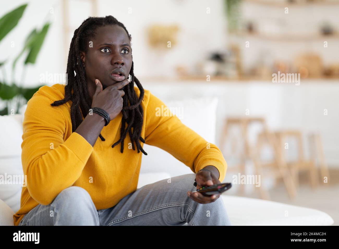 Amazed Young Black Guy Holding Remote Controller And Looking At Tv Screen Stock Photo