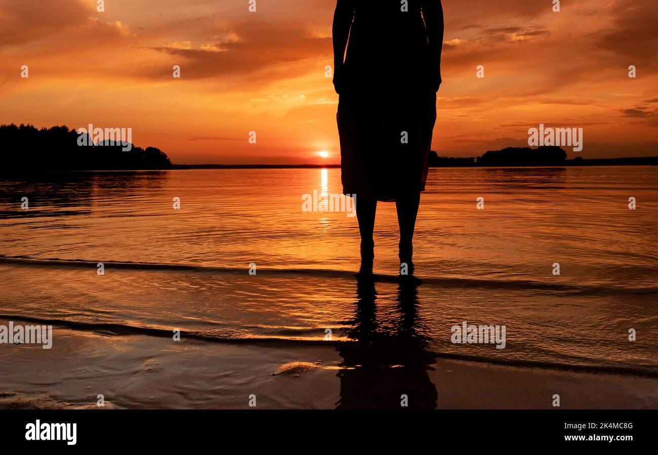 Women legs feet silhouette standing in water at sunset over lake. High quality photo Stock Photo
