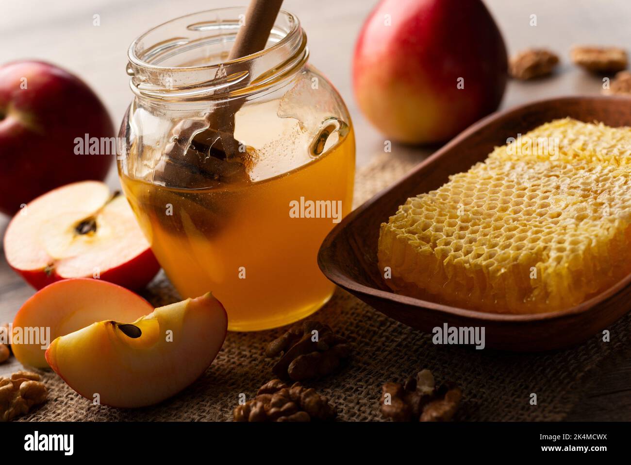 Mason jar with honey, honey dipper, red apples and walnuts