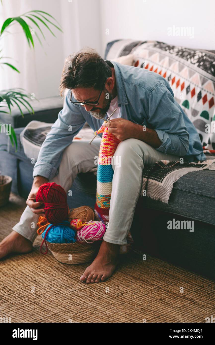 One man at home doing knit activity alone sitting on the sofa. Mature male people love knitting work for no stress hobby and relax time. Concept of Stock Photo