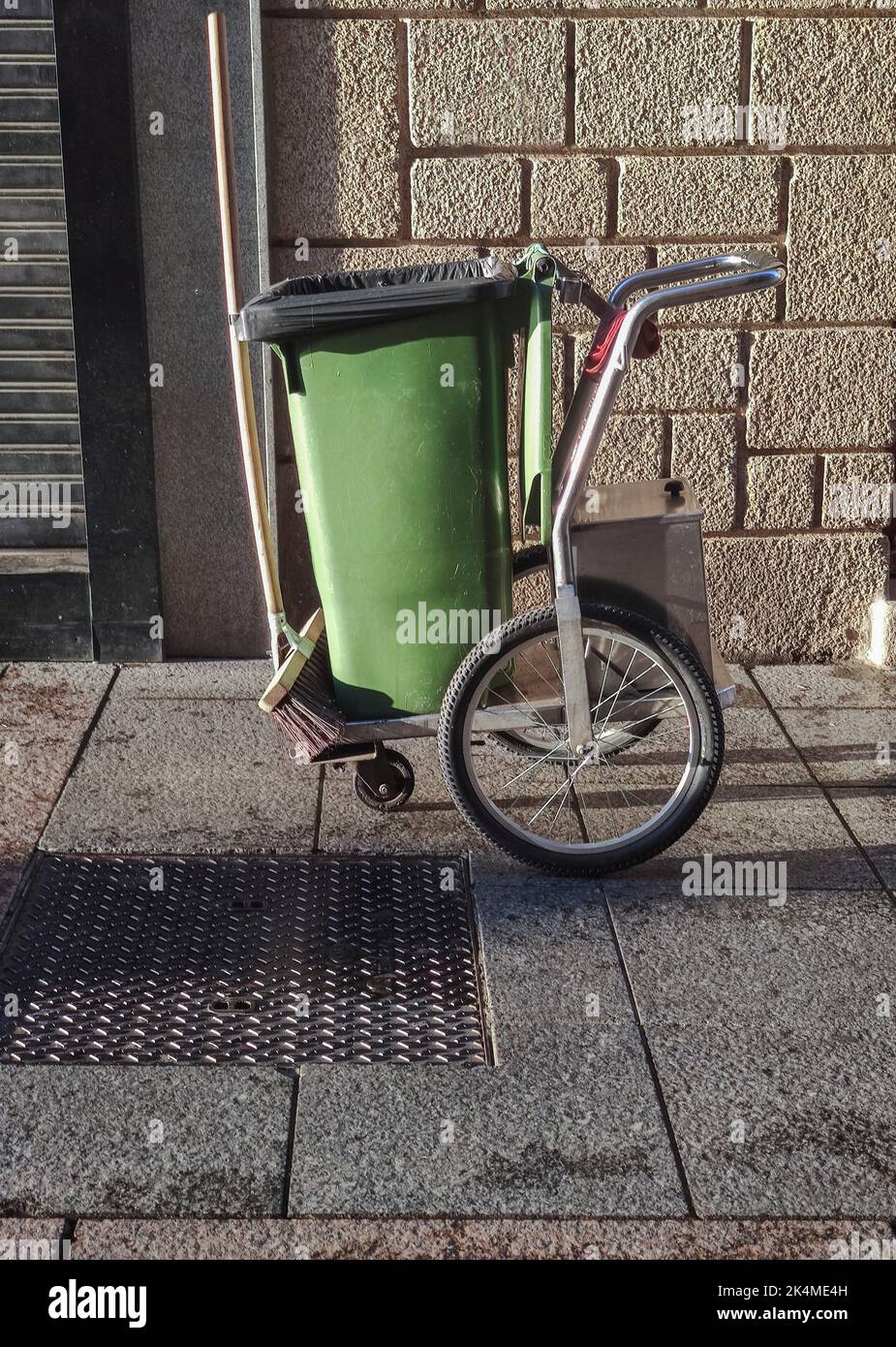 Street sweeper cart with green dumpster and sweep. Downtown background. Stock Photo