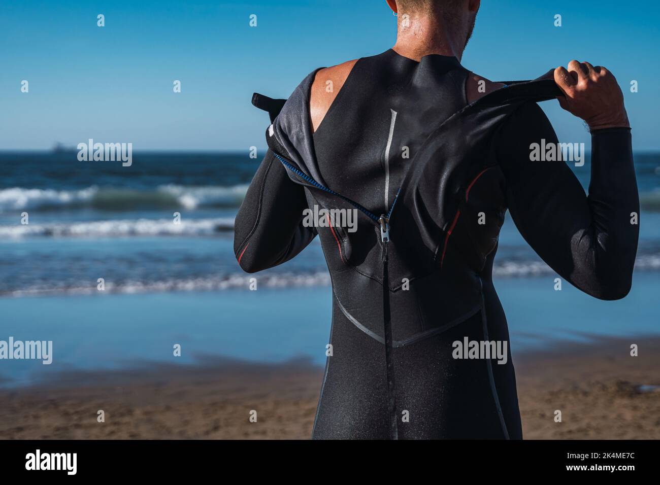 Man on the beach takes off his wet wetsuit after his surf lesson Stock