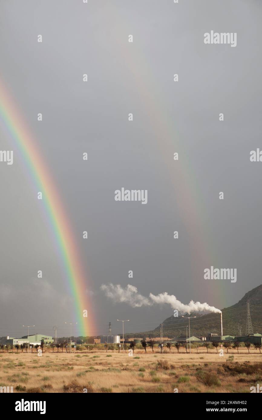 Double rainbow rising over an industrial area. Primary and secondary rainbows are visible. Stock Photo