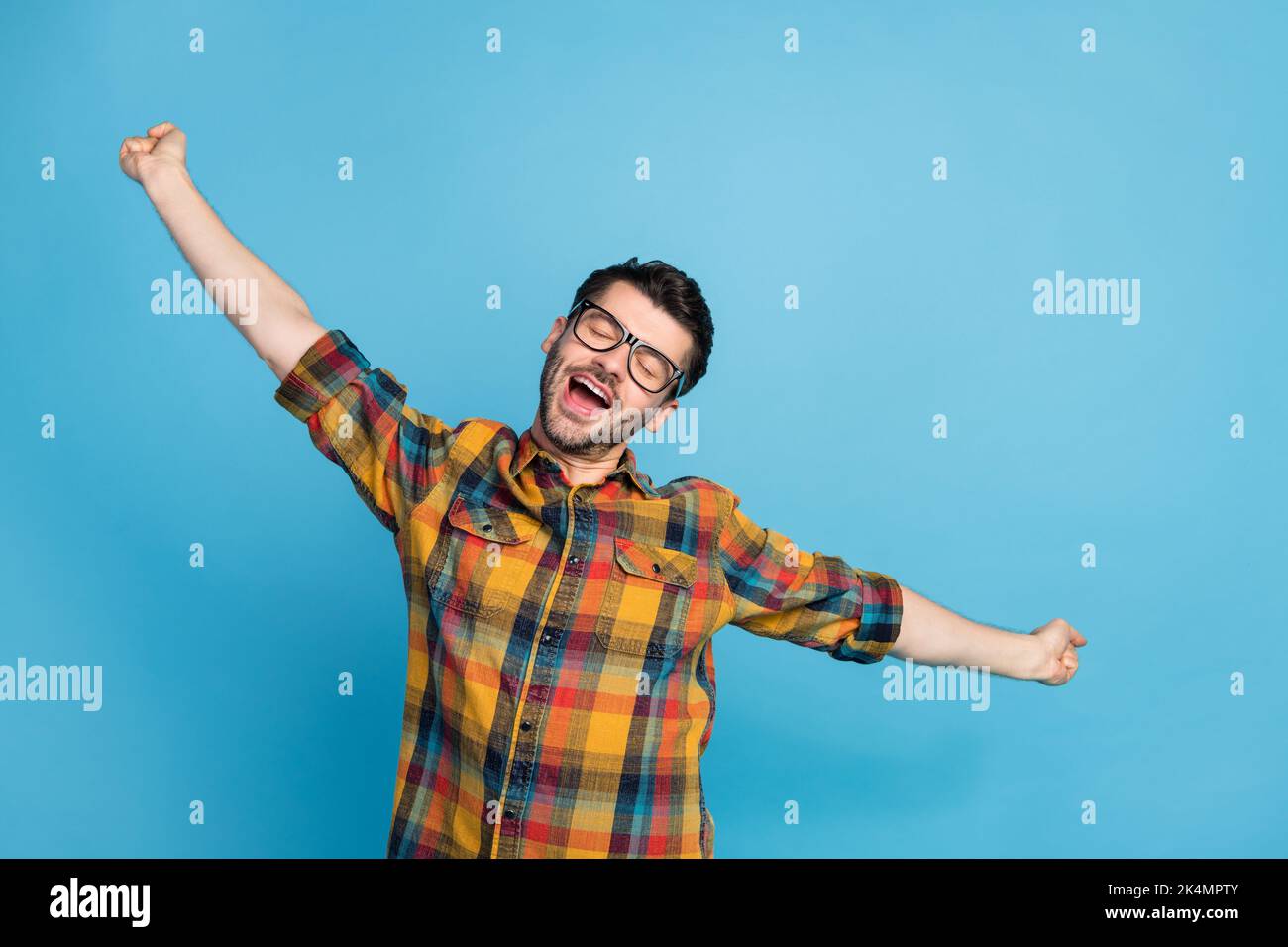 Photo of peaceful handsome man in eyewear dressed checkered shirt stretching slumbering closed eyes isolated on blue color background Stock Photo