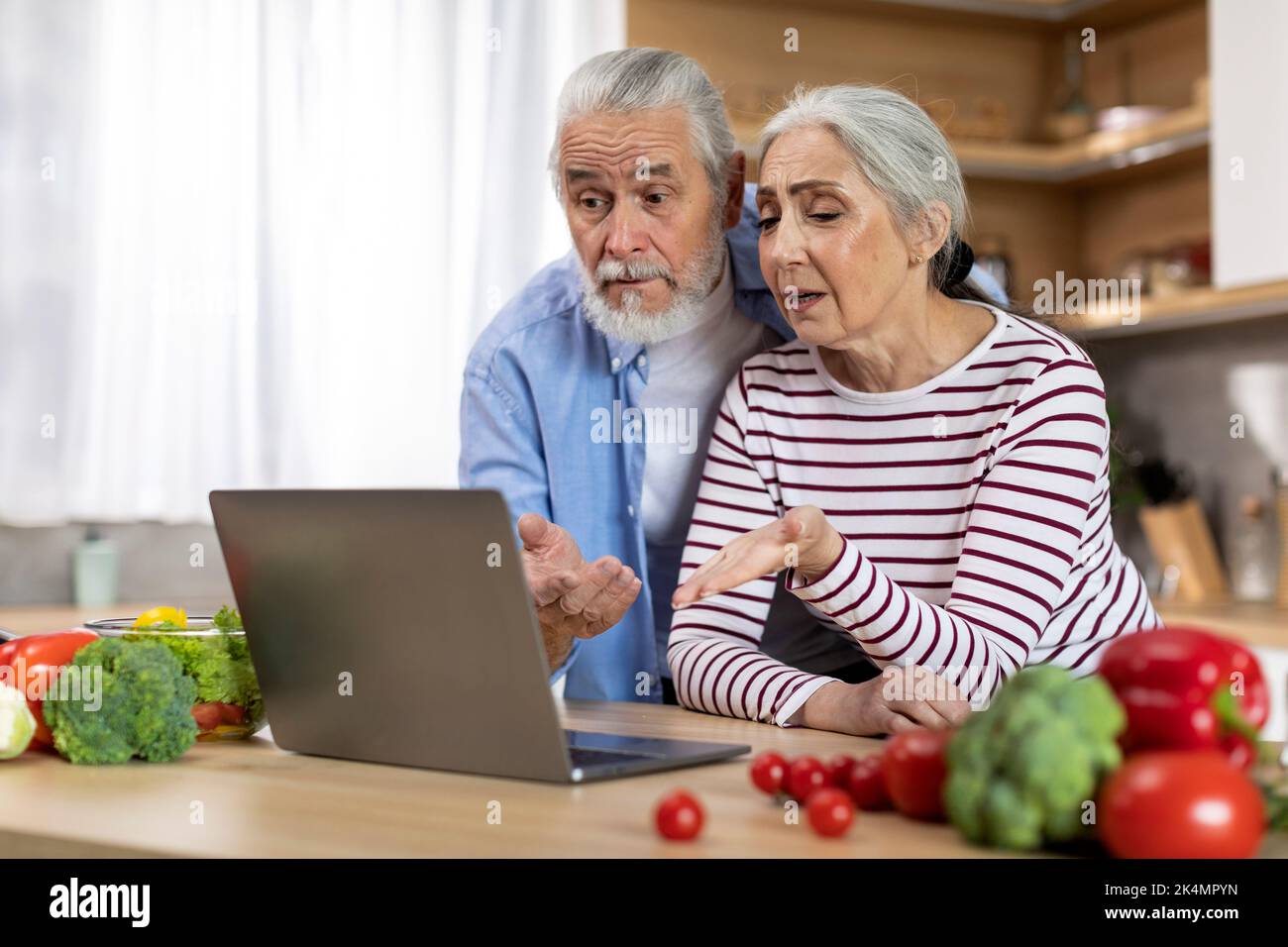 Confused Senior Spouses Suffering Problems With Laptop While Spending Time In Kitchen Stock Photo
