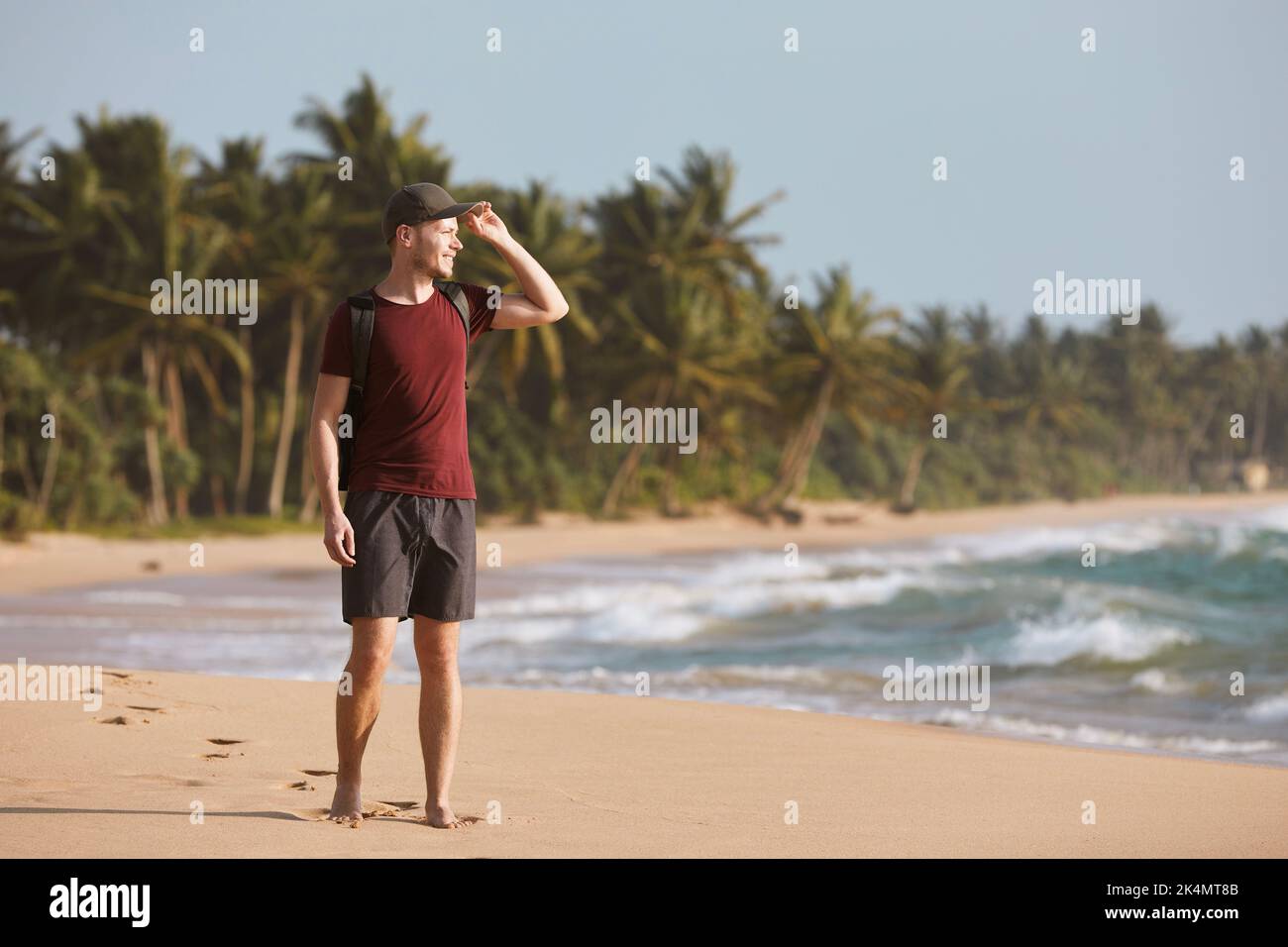 Happy man walking on idyllic sand beach against coast with palm trees in Sri Lanka. Stock Photo