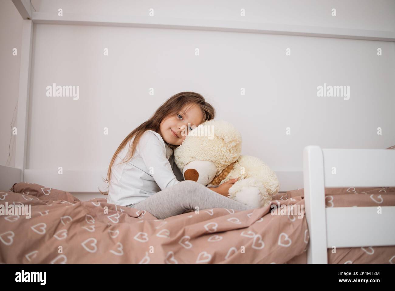 Cute little girl in pajama hugging her toy bear on the scandinavian ...