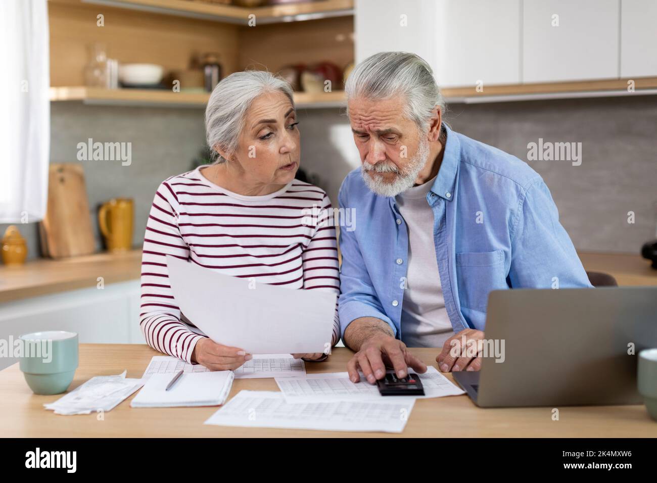 Elderly Spouses Calculating Family Expenses While Sitting On Table In Kitchen Stock Photo