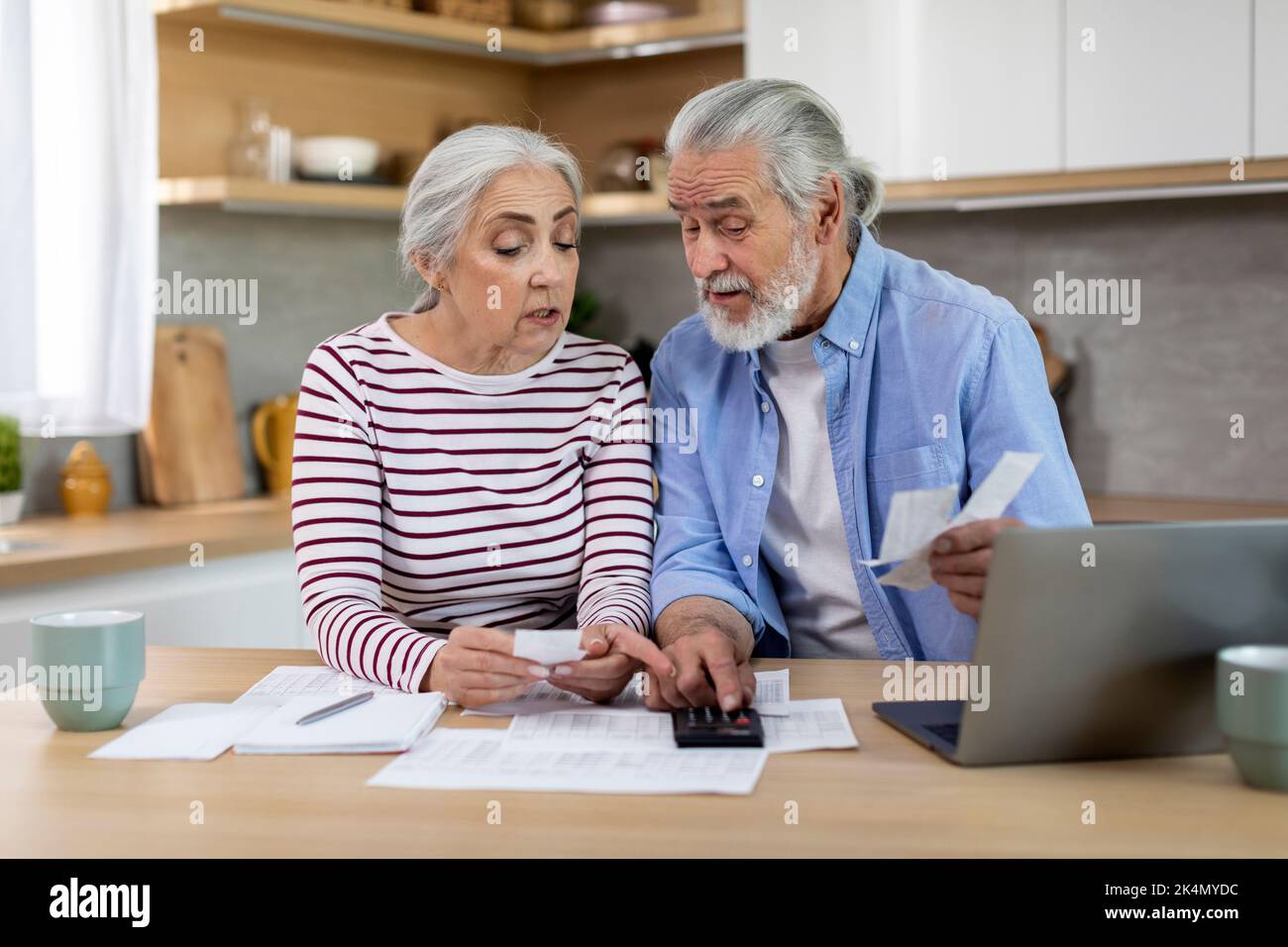 Senior couple sitting at table with papers and bills and using calculator Stock Photo