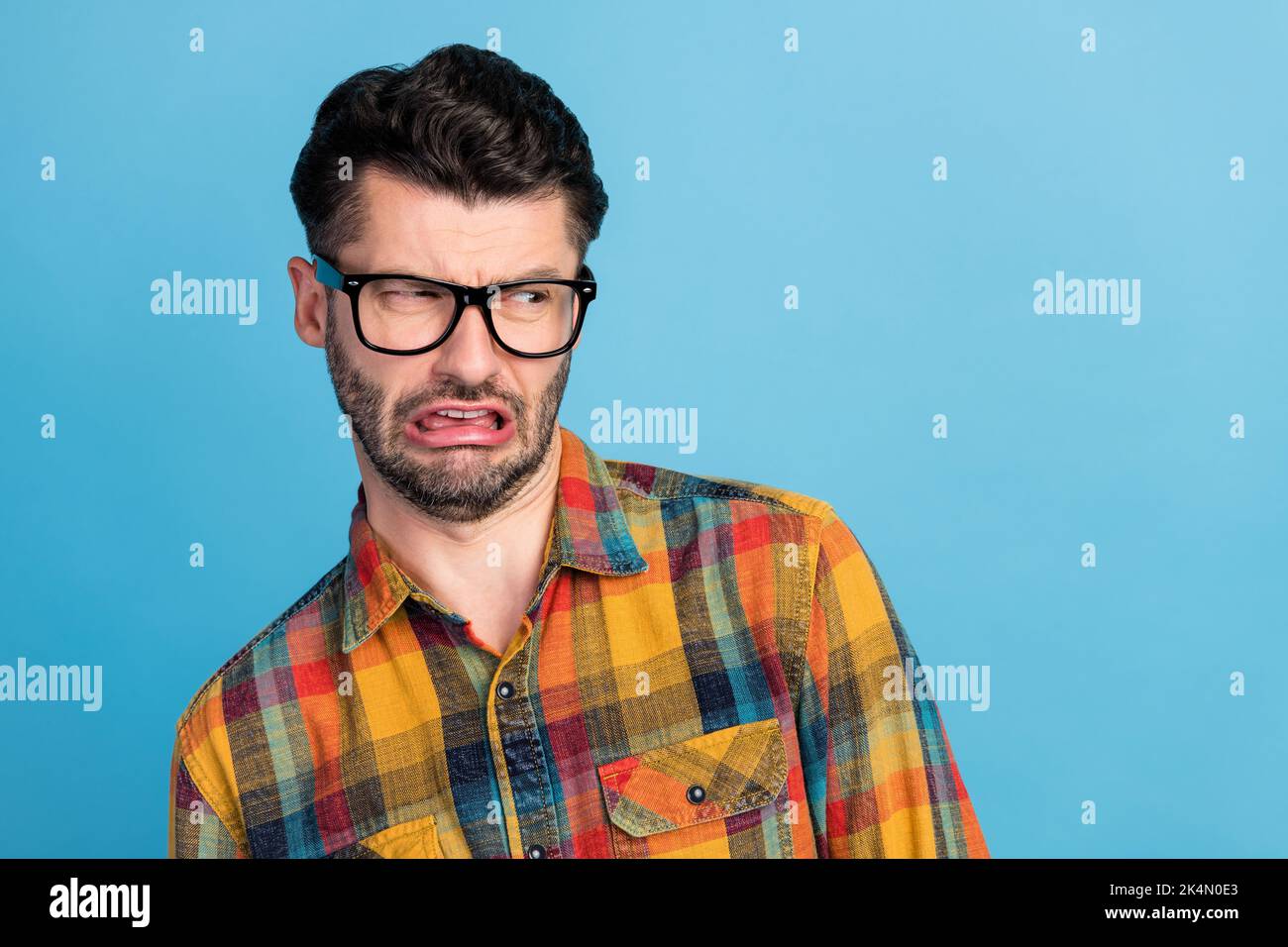 Photo of disgusted brunet guy look empty space wear spectacles plaid shirt isolated on blue color background Stock Photo